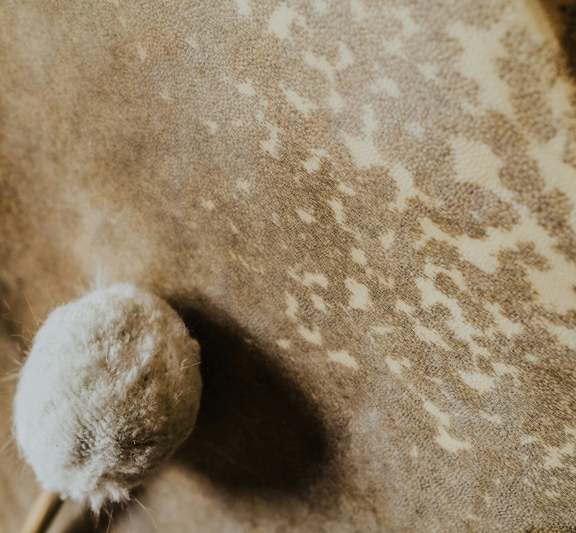 Extreme Nahaufnahme der strukturierten Oberfläche eines handgefertigten Trommelfells, auf der ein weicher, gefilzter Schlägelkopf ruft. Die Komposition, mit dem Schlägel im Fokus und einem sanften Schatten, betont die Kraft des Klangs und die Vorbereitung auf eine Klangheilungssitzung im LIVANDA Zentrum Parin.