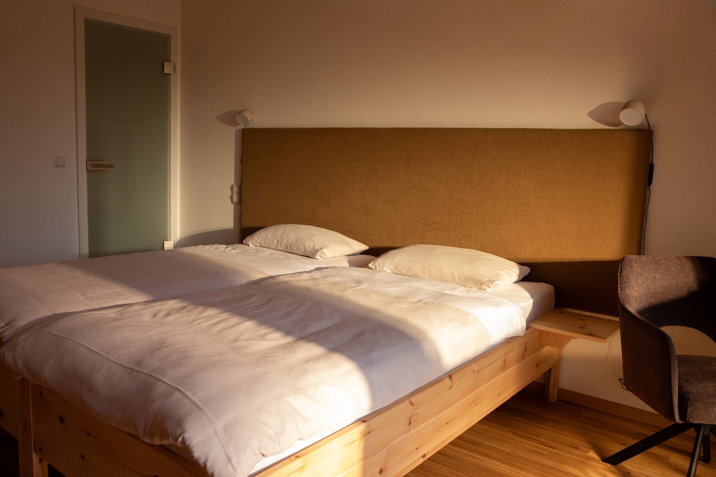 Ein einladender Blick in eine schlichte, helle Unterkunft im LIVANDA. Man sieht mehrere gemütlich hergerichtete Betten, die zum Ausruhen einladen.