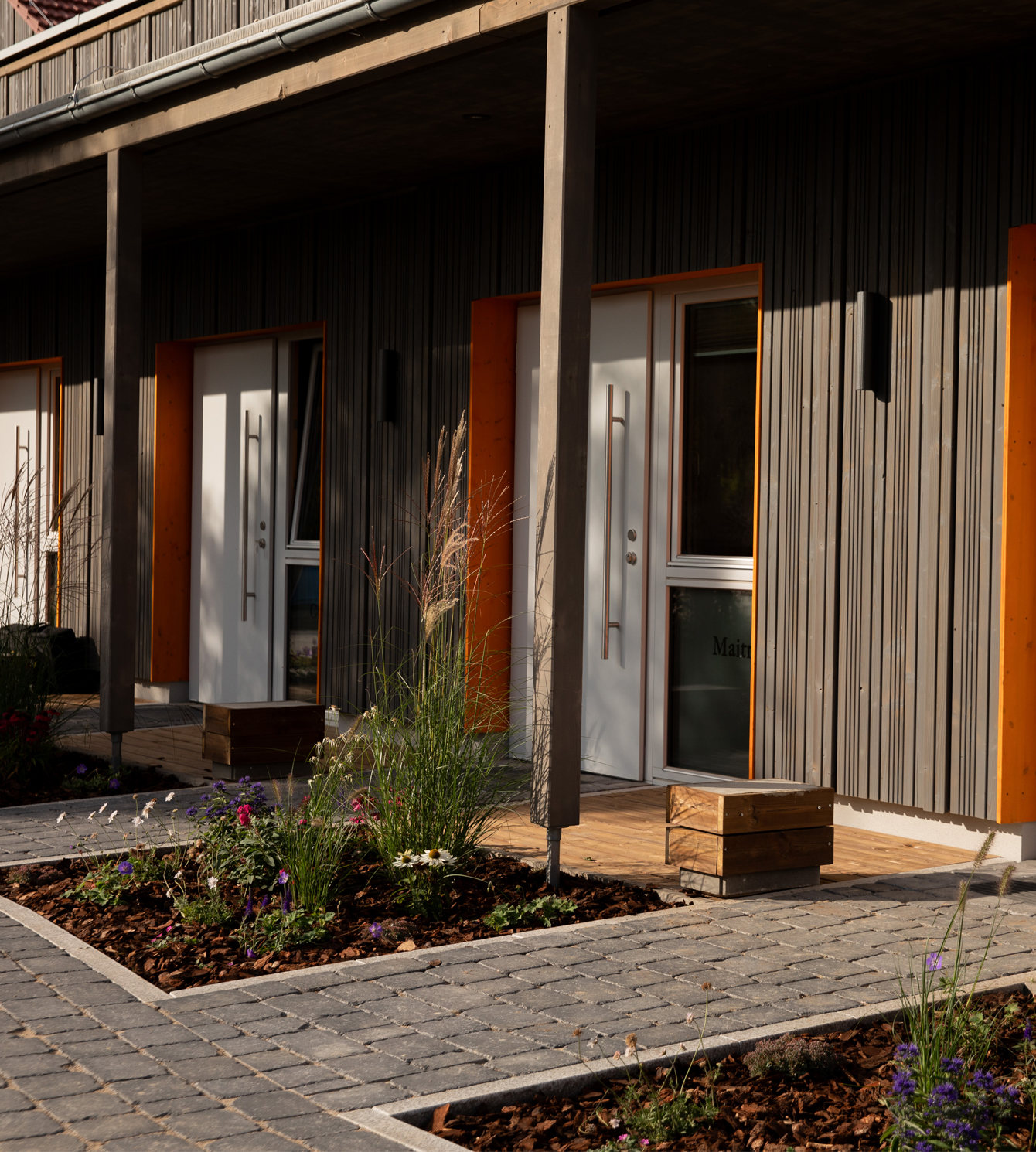 Innenansicht eines lichtdurchfluteten Apartments im LIVANDA. Hohe Holzdecken, helle Wände und ein großer Fensterfront-Blick direkt ins Grüne schaffen eine Atmosphäre von Ruhe und Geborgenheit. Eine gemütliche Sitzecke und ein Esstisch mit frischen Tulpen laden zum Ankommen und Entspannen ein.