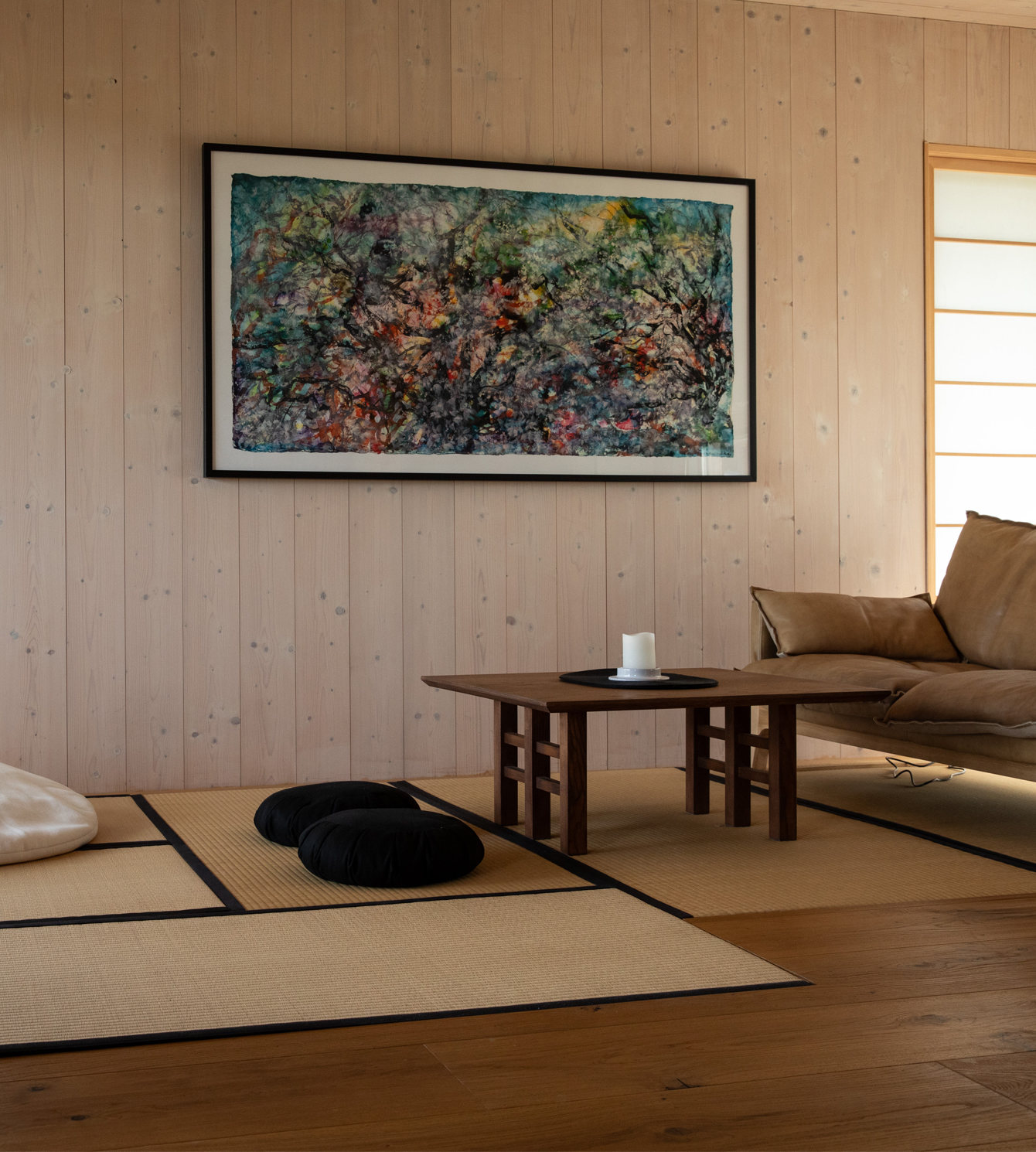 Außenansicht eines modernen Ferienhauses im warmen Abendlicht. Die dunkle Holzfassade, das rote Ziegeldach und die großen Glasfronten strahlen Gemütlichkeit und Naturverbundenheit aus. Blühende Gräser im Vordergrund und ein Kiesweg führen zum einladenden Eingang.