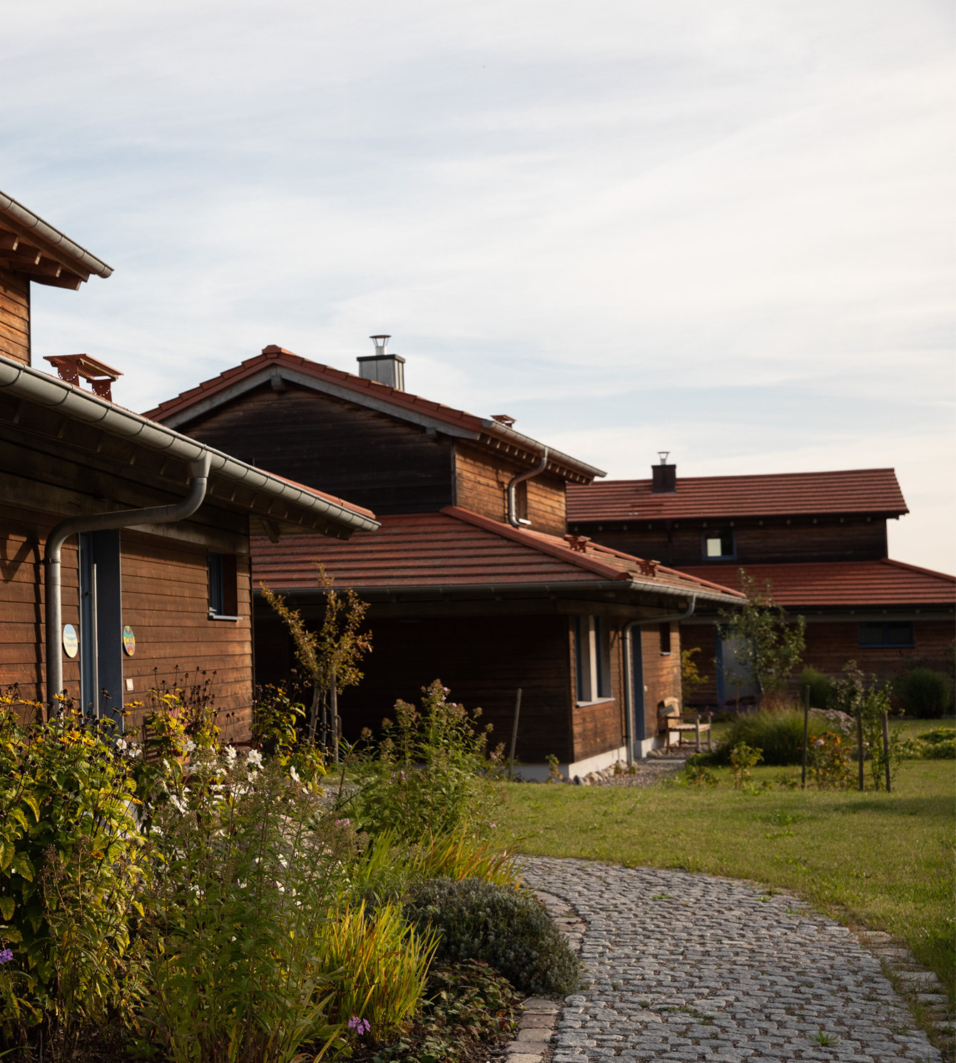 Eine idyllische Gesamtansicht des LIVANDA Ferienhauses, eingebettet in die weite, grüne Landschaft Mecklenburgs unter klarem blauem Himmel. Die Architektur aus dunklem Holz fügt sich harmonisch in die Umgebung ein und verspricht einen friedlichen Rückzugsort.
